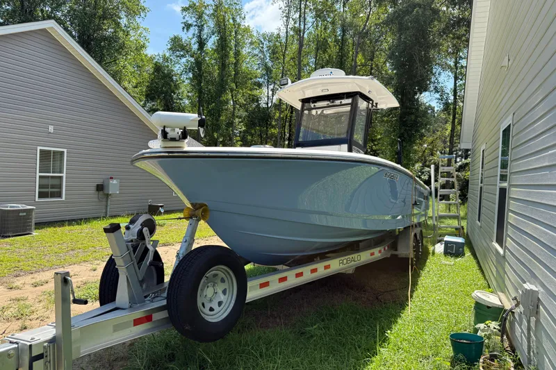 Slide: The Image of 2022 Robalo 266 Cayman boat on trailer beside house, surrounded by greenery. - 0