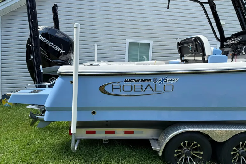 Slide: The Image of 2022 Robalo 266 Cayman boat on trailer with Mercury engine, parked on grass. - 2