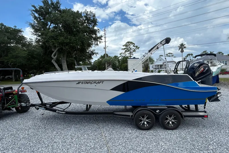 Slide: The Image of 2023 Starcraft SVX 231 OB DH boat on trailer, parked outdoors under a blue sky. - 8