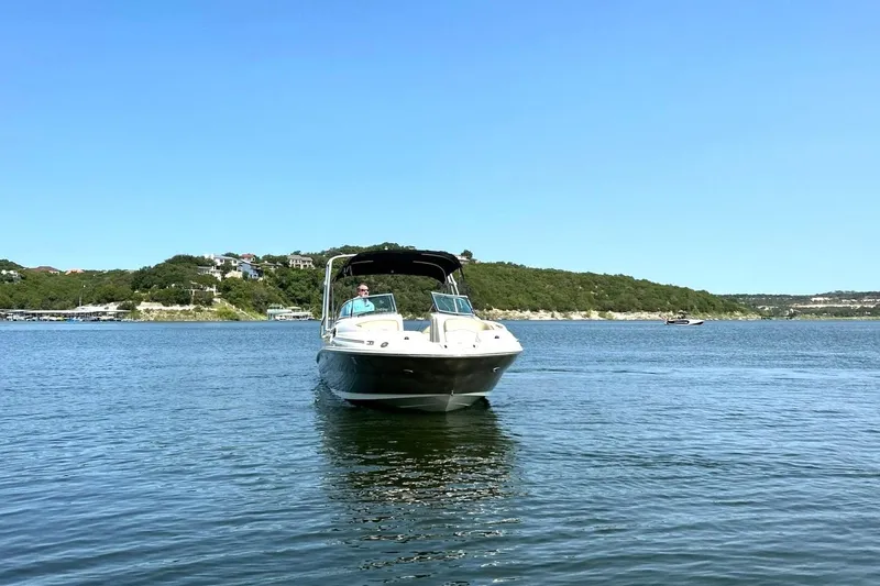Slide: The Image of 2006 Sea Ray 240 Sundeck boat on a serene lake with scenic hillside backdrop. - 10
