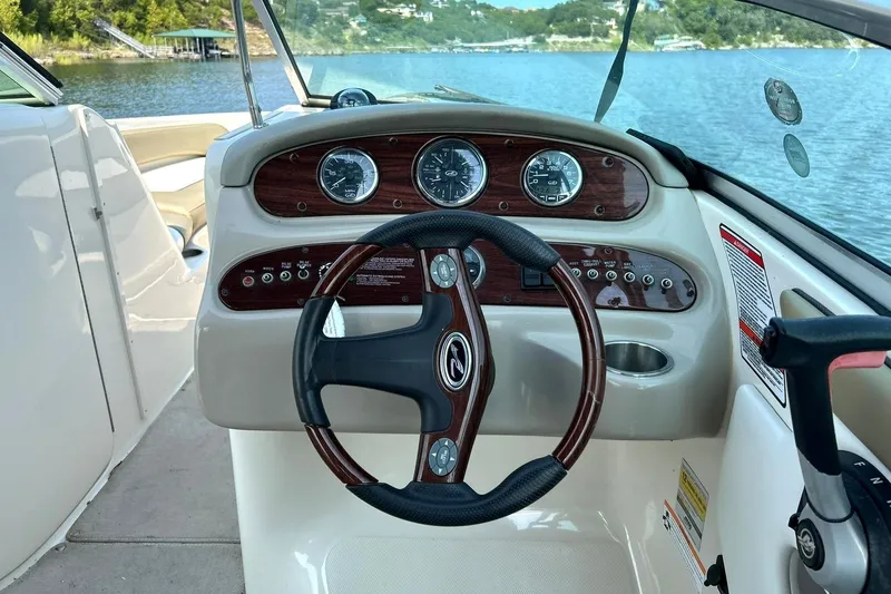 Slide: The Image of 2006 Sea Ray 240 Sundeck dashboard with steering wheel, gauges, and controls on a lake. - 28