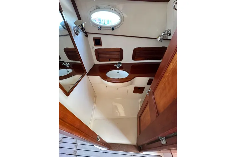 Slide: The Image of Hinckley Picnic Boat 36 bathroom interior, featuring wood accents and a round porthole window. - 25
