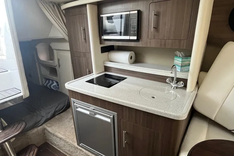 Slide: The Image of 2020 Rinker 290 EX boat interior with kitchenette, featuring microwave, sink, and storage cabinets. - 21