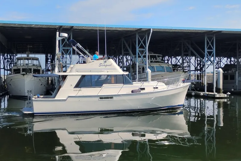 The Image of 1985 Mainship 34 Mk III boat docked in a marina, reflecting on calm water. - 0