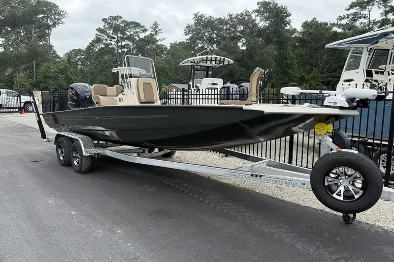 Slide: The Image of 2026 Xpress H22B boat on trailer, parked outdoors, surrounded by trees and other boats. - 2