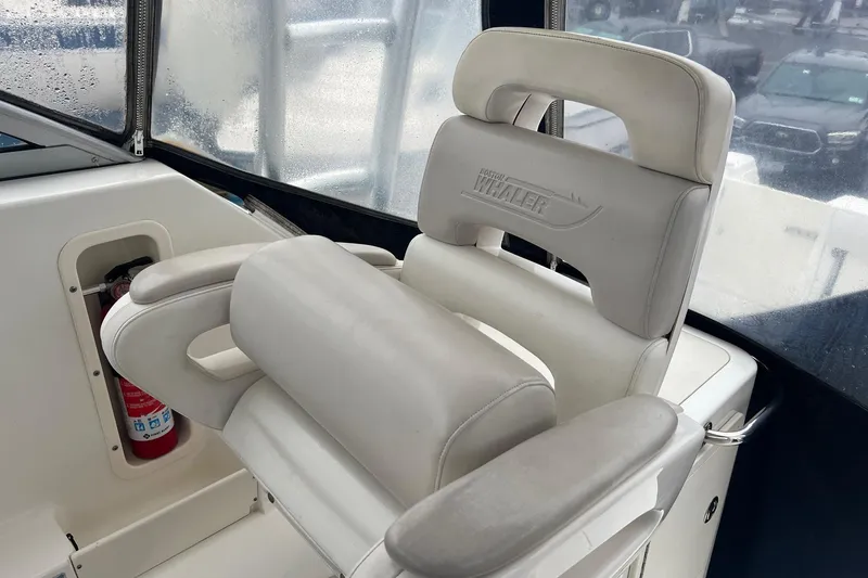 Slide: The Image of 2005 Boston Whaler 305 Conquest helm seat with logo, featuring white cushioned design. - 24