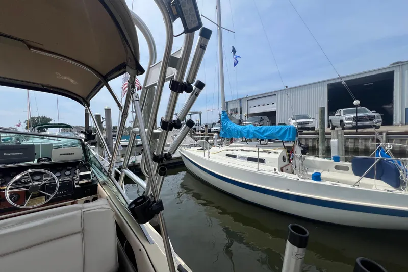 Slide: The Image of 1986 Sea Ray 270 Amberjack at marina, alongside sailboat, with docked vehicles in background. - 15
