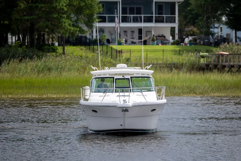 Slide: The Image of 2004 Tiara Yachts 3200 Open cruising on a serene river near a lush riverside home. - 2