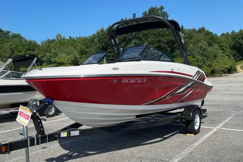 Slide: The Image of 2024 Bayliner VR5 Bowrider I/O boat on trailer in parking lot, red and white design. - 1