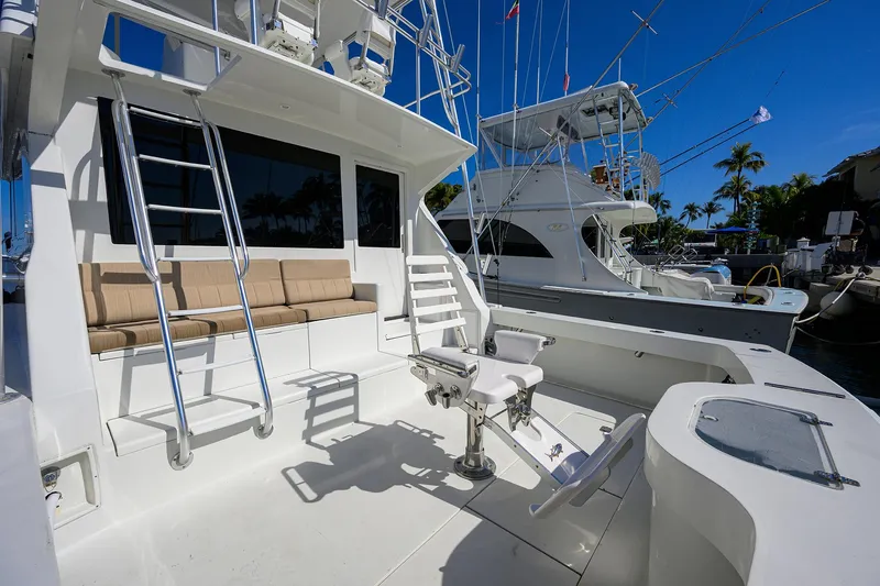 Slide: The Image of 1998 Viking 53 Convertible yacht deck with seating and fishing chair, docked under clear blue sky. - 12