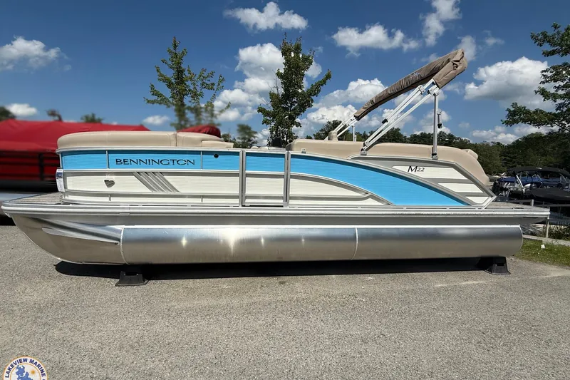 Slide: The Image of 2025 Bennington 22ML pontoon boat with blue accents, parked outdoors under a clear sky. - 2