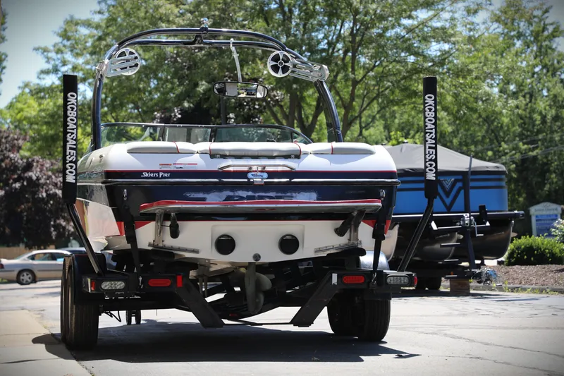 Slide: The Image of 2008 Malibu 21 vRide boat on trailer, parked outdoors with trees in background. - 2