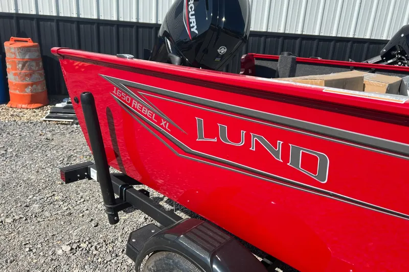 Slide: The Image of Red 2026 Lund 1650 Rebel XL Sport boat with Mercury engine, parked outdoors. - 3