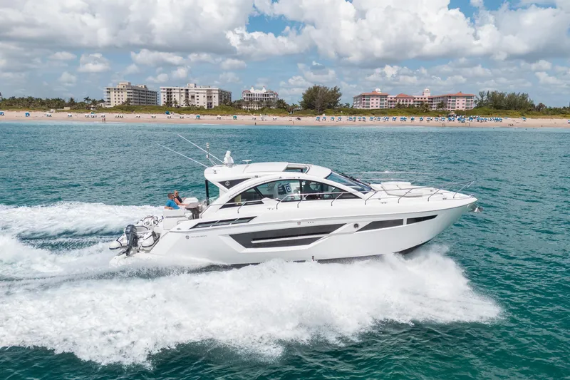 Slide: The Image of 2019 Cruisers Yachts Cantius sailing near a beach with buildings in the background. - 56