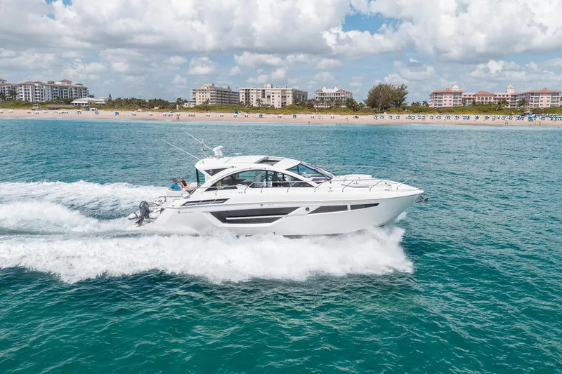 Slide: The Image of 2019 Cruisers Yachts Cantius cruising on clear blue water near a sandy beach. - 60