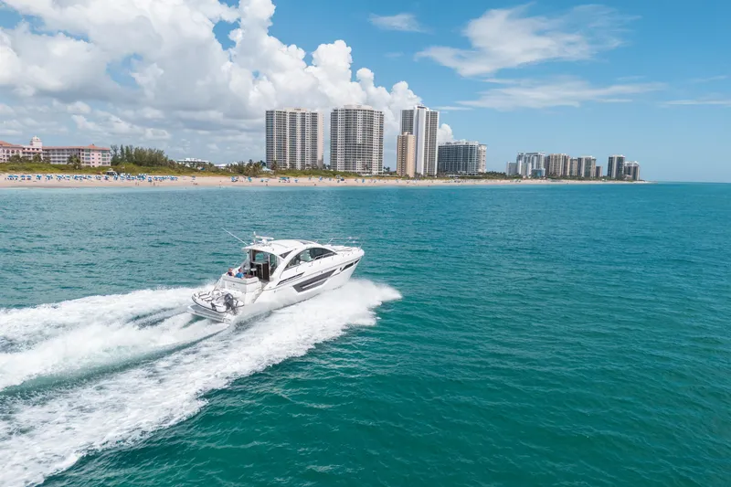 Slide: The Image of 2019 Cruisers Yachts Cantius cruising near a coastal city skyline under a clear blue sky. - 65