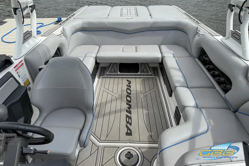 Slide: The Image of 2021 Moomba Craz boat interior with gray seating and branded flooring, docked by water. - 11