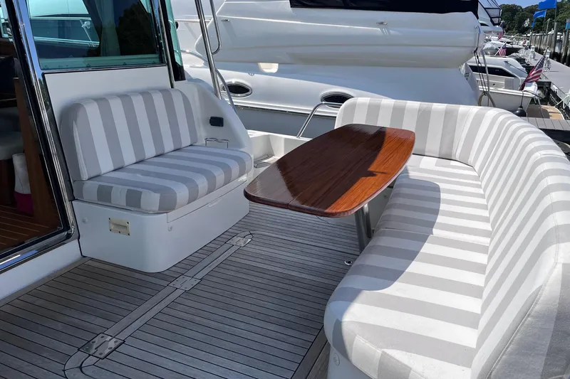 Slide: The Image of 2022 Sabre 48 Salon Express yacht deck with striped seating and wooden table, overlooking serene water. - 7