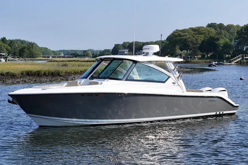 The Image of 2018 Pursuit DC 295 Dual Console boat on calm water, surrounded by lush greenery. - 0