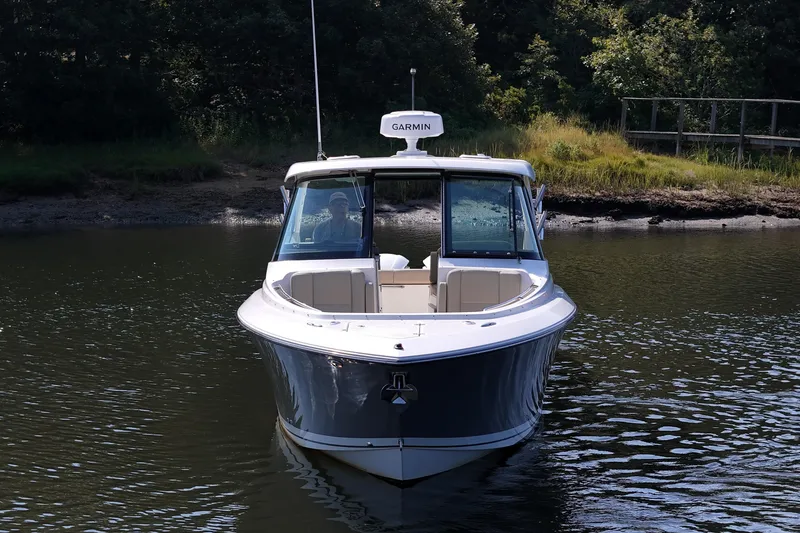 Slide: The Image of 2018 Pursuit DC 295 Dual Console boat on calm water, surrounded by greenery. - 11