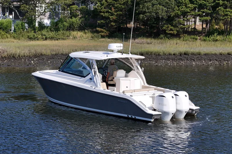 Slide: The Image of 2018 Pursuit DC 295 Dual Console boat cruising on a calm river near a wooded shoreline. - 3