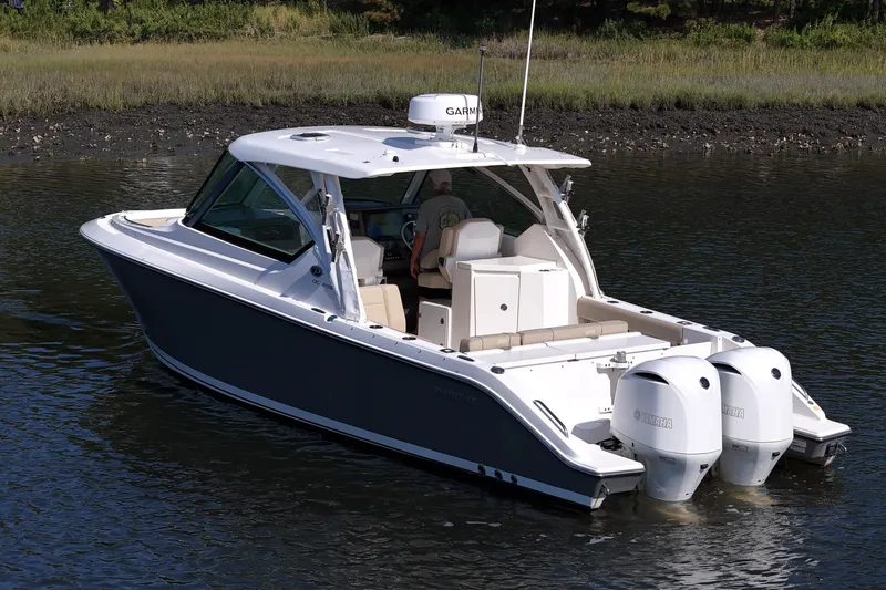 Slide: The Image of 2018 Pursuit DC 295 Dual Console boat on calm water with twin Yamaha engines. - 4