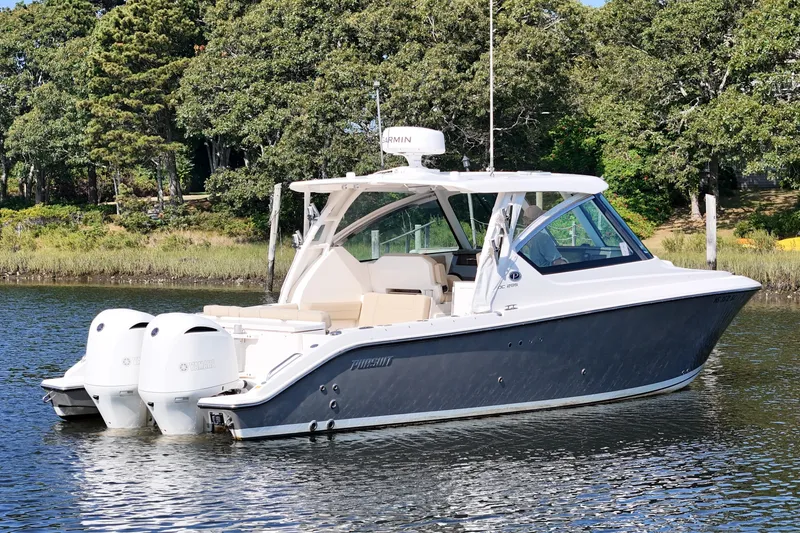 Slide: The Image of 2018 Pursuit DC 295 Dual Console boat on calm water, surrounded by lush greenery. - 7
