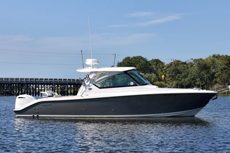 Slide: The Image of 2018 Pursuit DC 295 Dual Console boat on calm water near a bridge. - 8
