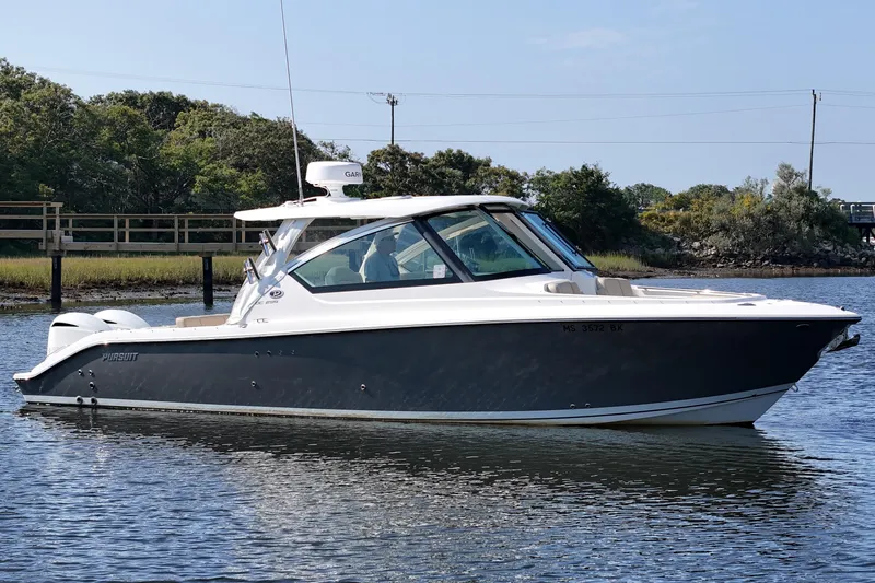 Slide: The Image of 2018 Pursuit DC 295 Dual Console boat on calm water, surrounded by lush greenery. - 9