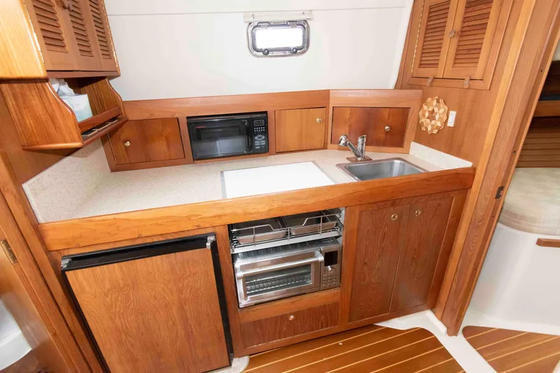 Slide: The Image of 2002 Mainship Pilot 34 Sedan galley with wood cabinetry, sink, microwave, and compact refrigerator. - 19