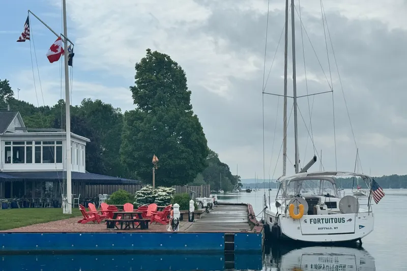 Slide: The Image of Jeanneau Sun Odyssey 410 sailboat docked by a lakeside house with flags. - 3