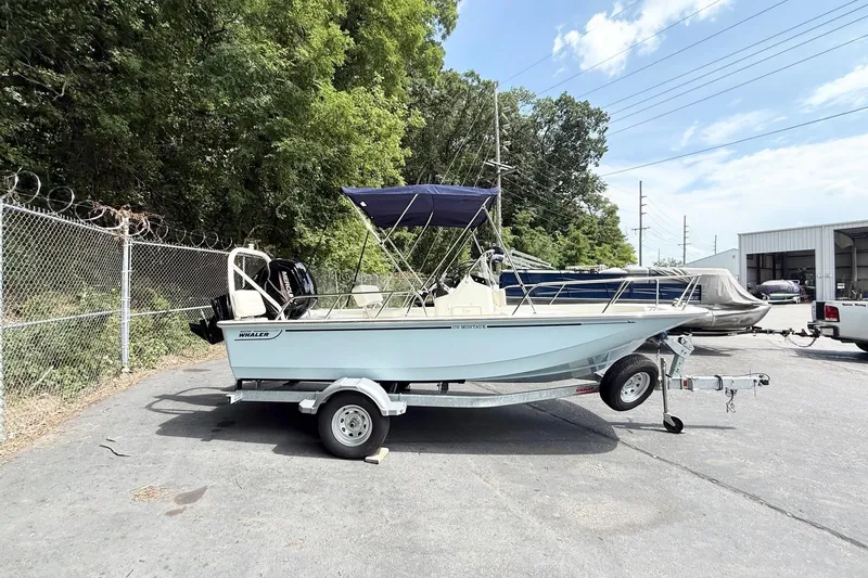 The Image of 2026 Boston Whaler 170 Montauk boat on trailer, parked outdoors near trees and fence. - 0