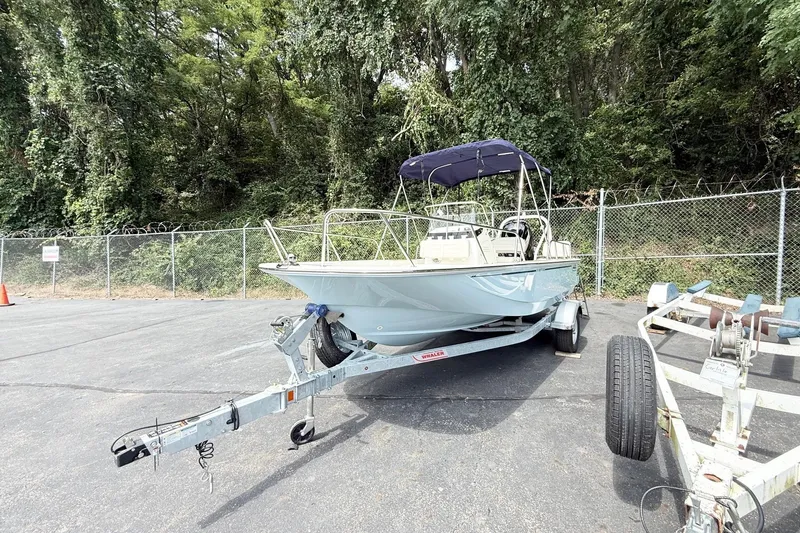Slide: The Image of 2026 Boston Whaler 170 Montauk boat on trailer, parked near a fence with trees in background. - 3