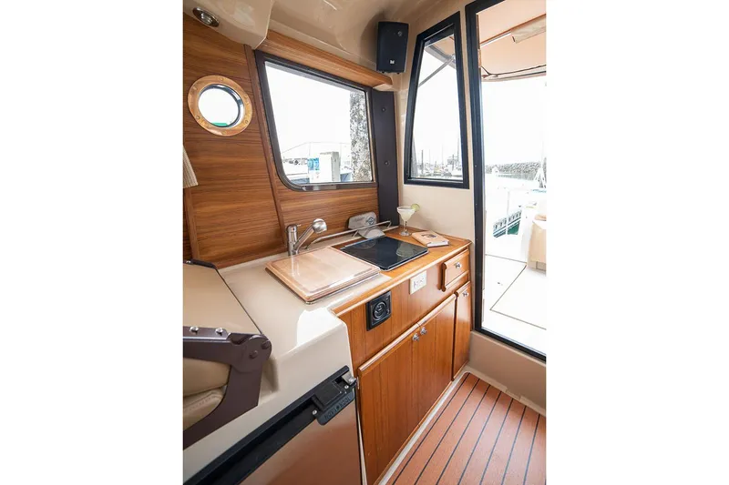 Slide: The Image of Manufacturer Provided Image: Interior of 2025 Ranger Tugs R-23 boat with compact kitchen and wooden cabinetry. - 16