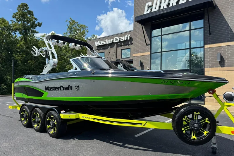 The Image of 2015 MasterCraft X30 boat with green accents on a trailer, parked outside a dealership. - 1