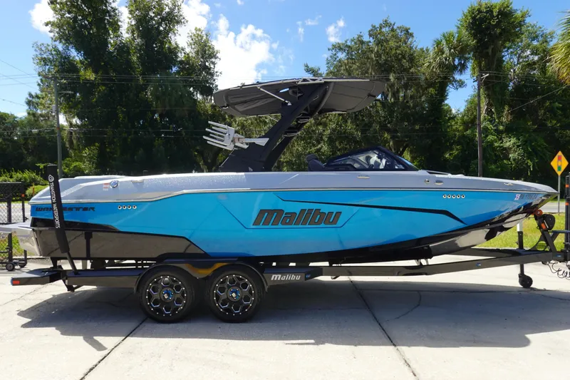 Slide: The Image of 2021 Malibu Wakesetter 25 LSV boat on trailer, vibrant blue design, parked outdoors. - 4