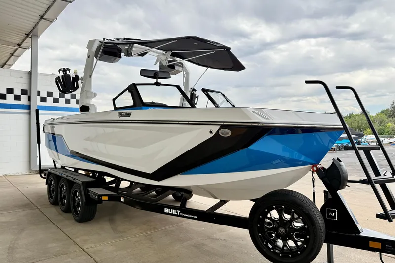 Slide: The Image of 2025 Nautique Super Air Nautique GS24 boat on trailer, white and blue design, parked outdoors. - 9