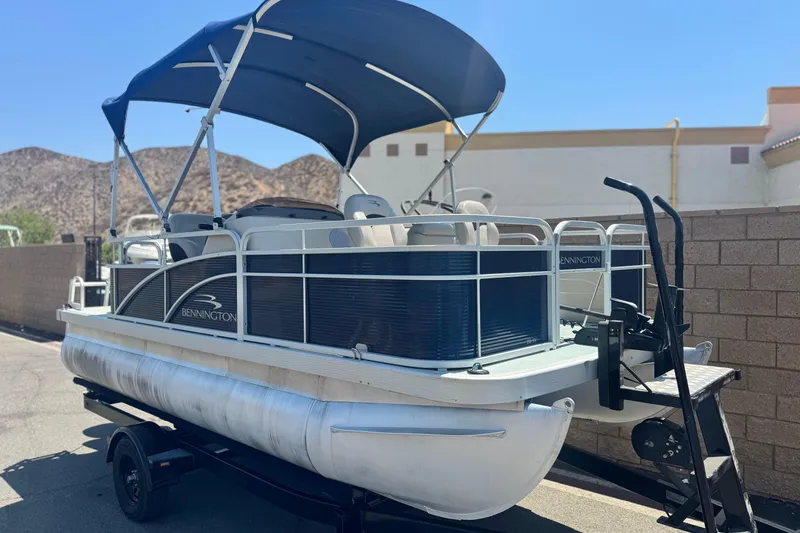 Slide: The Image of 2019 Bennington 188 SV pontoon boat with blue canopy on trailer, parked outdoors. - 1