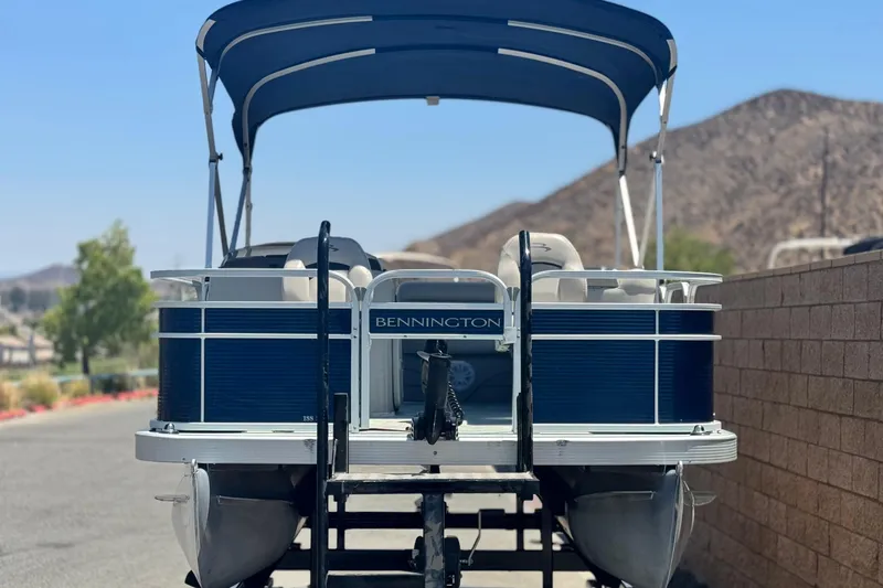 Slide: The Image of 2019 Bennington 188 SV pontoon boat with canopy, parked near mountains. - 2
