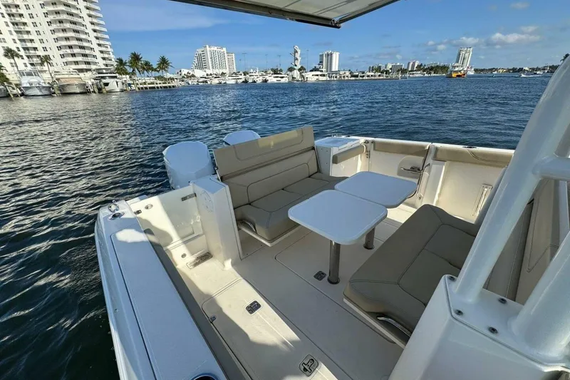 Slide: The Image of 2020 Pursuit S 328 Sport boat interior with seating and tables, docked near waterfront buildings. - 6