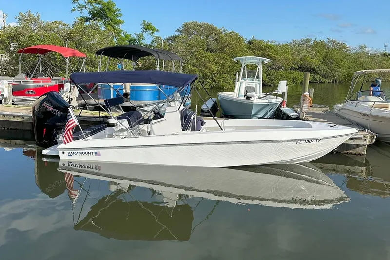 Slide: The Image of A 2022 Paramount 21 boat docked on calm water, featuring a sleek design and American flag. - 0