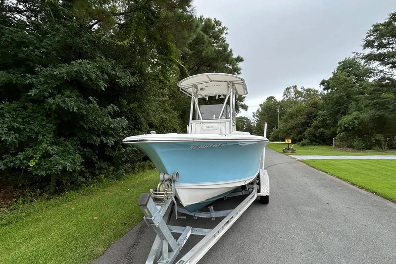 Slide: The Image of 2016 Sea Hunt Ultra 210 boat on trailer, parked on a tree-lined road. - 17