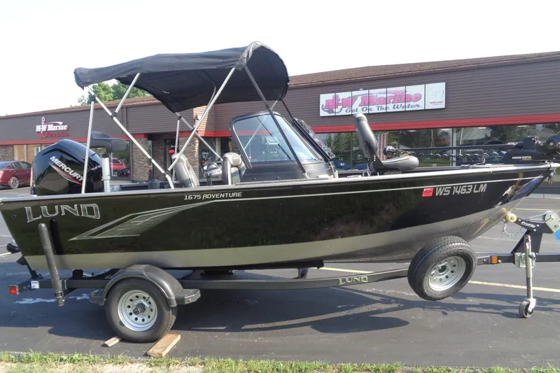 Slide: The Image of 2022 Lund 1675 Adventure Sport boat on trailer, parked outside a marine store. - 2