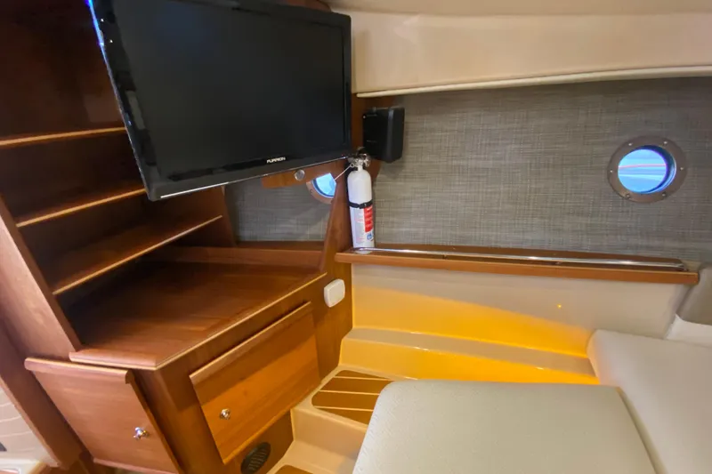 Slide: The Image of 2019 Ranger Tugs R-29 S interior with TV, wooden shelves, and porthole window. - 64