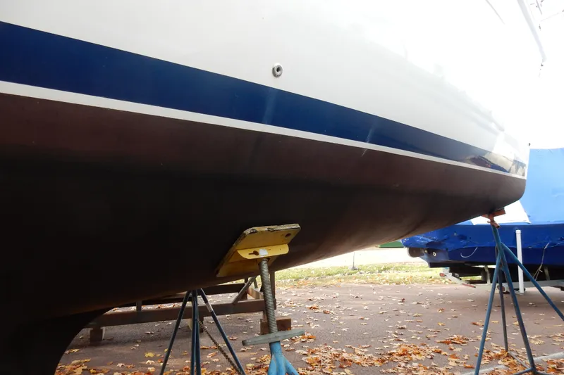 Slide: The Image of 2011 Hunter 39 sailboat hull on stands, blue stripe, autumn leaves on ground. - 69