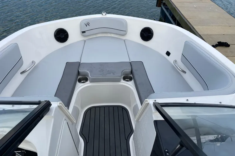 Slide: The Image of 2023 Bayliner VR5 boat interior with gray seating and cup holders, docked by the water. - 8