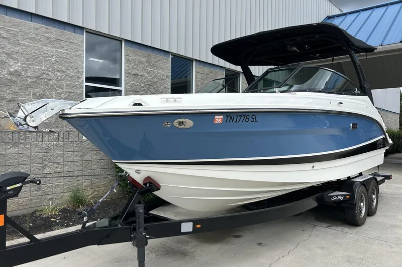 Slide: The Image of 2023 Sea Ray SLX 260 boat on trailer, blue and white exterior, parked outside building. - 2