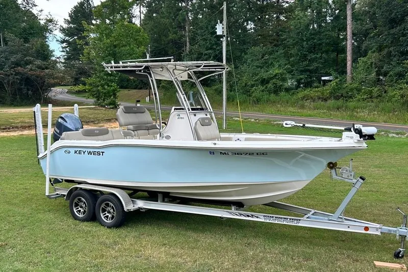 Slide: The Image of 2022 Key West 219 FS boat on trailer, parked on grass with trees in background. - 0