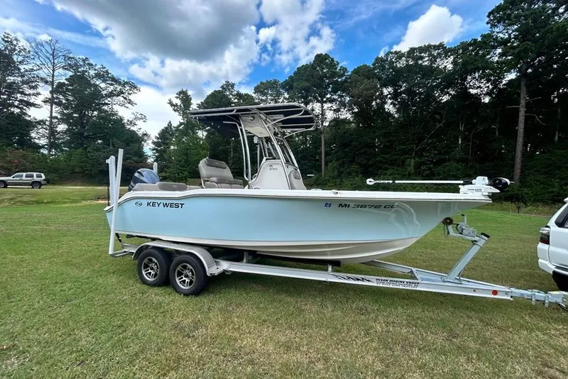 Slide: The Image of 2022 Key West 219 FS boat on trailer, parked on grassy field under cloudy sky. - 1