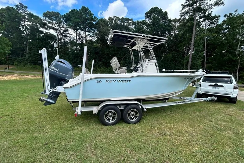 Slide: The Image of 2022 Key West 219 FS boat on trailer, parked on grass beside a white SUV. - 2